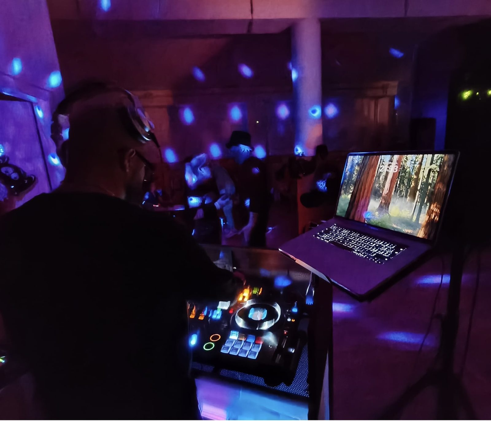 Fabrix DJ alla console con luci blu e viola e gli invitati dietro